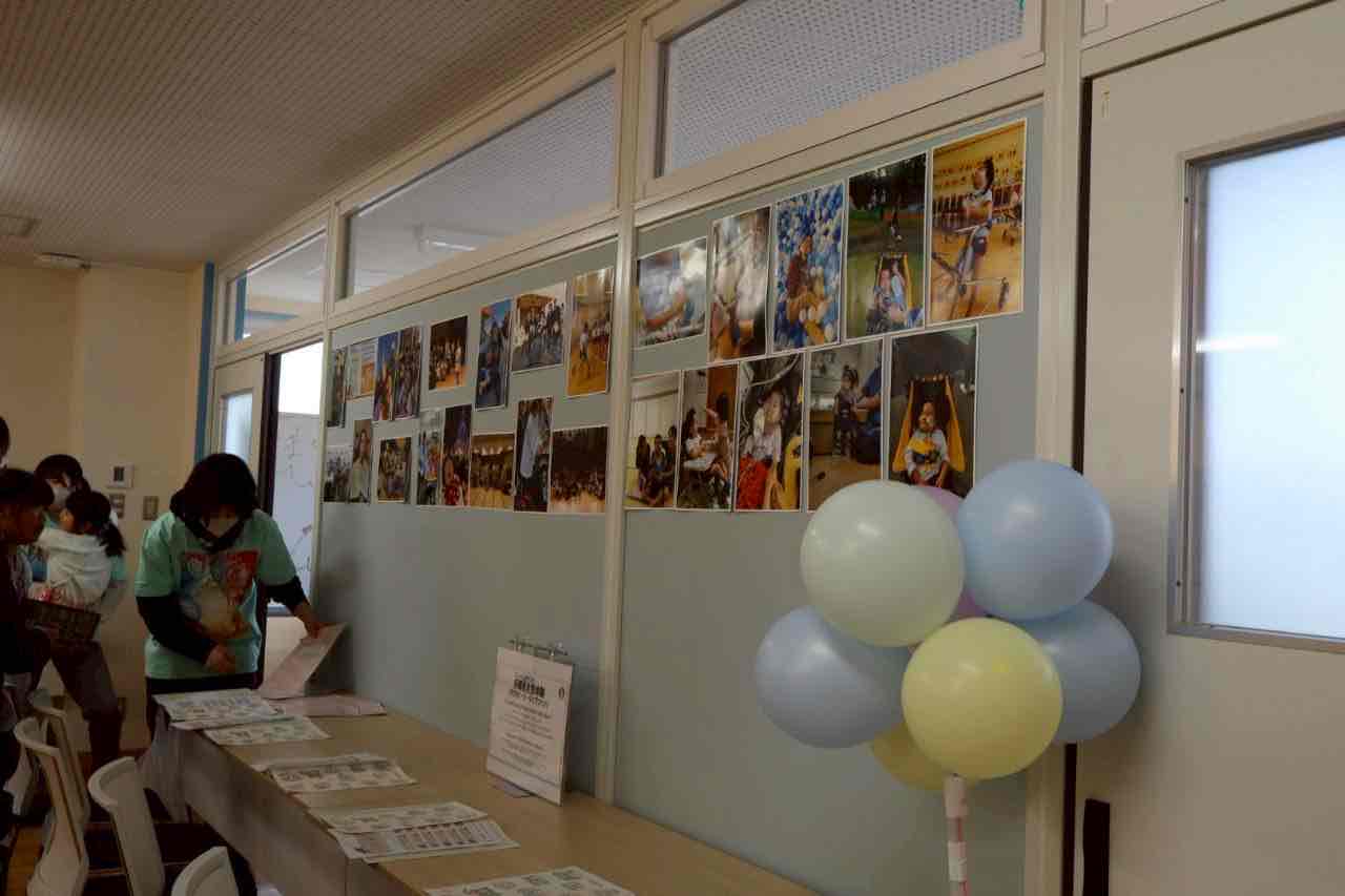 活動写真を掲示した会場で、人たちがテーブルを囲む地域イベントの様子
