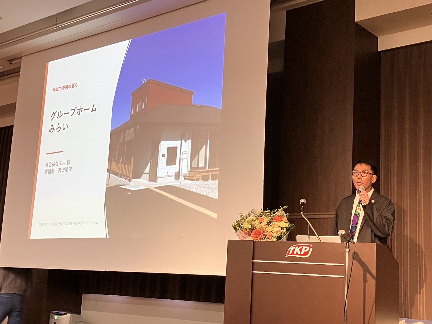 グループホームみらいの紹介スライドを使って登壇している場面
